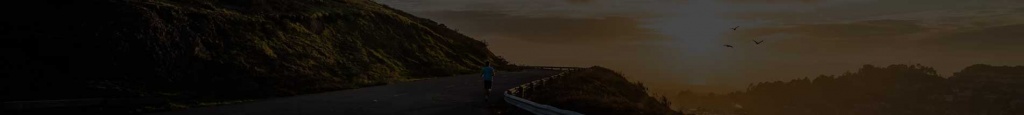 Corredor con camiseta azul en una carretera costera junto a un acantilado al atardecer, aves en el cielo.