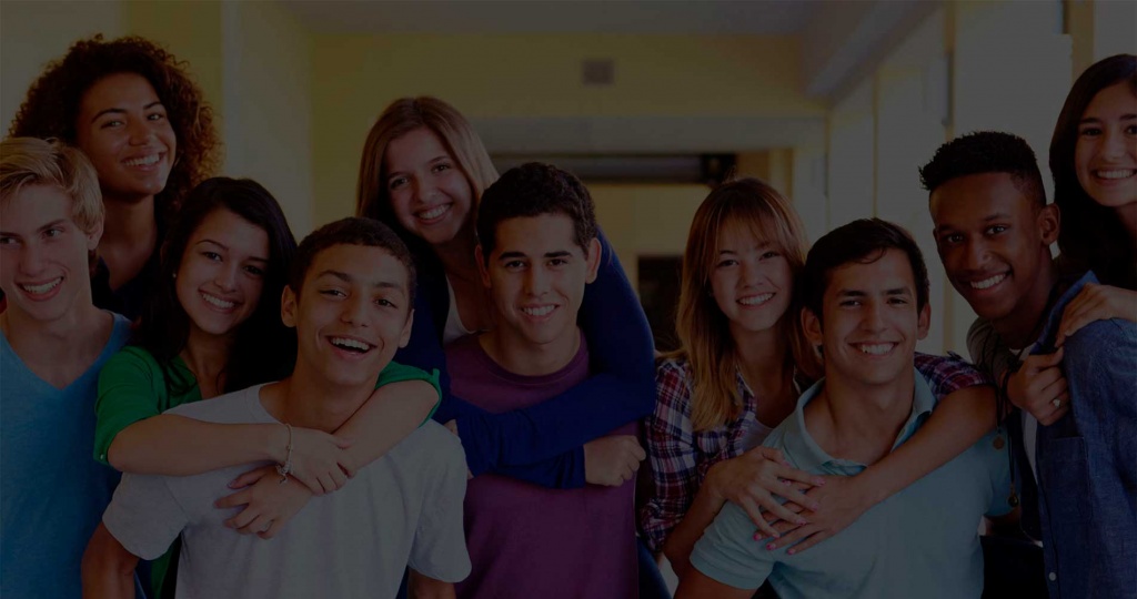 Grupo de adolescentes sonrientes y diversos abrazándose en un pasillo escolar, con ropa casual.