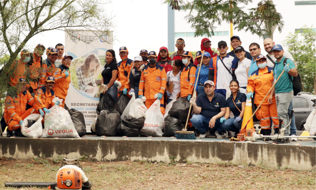 Equipo de voluntarios y trabajadores en uniformes naranjas posando con bolsas de basura y herramientas de limpieza.