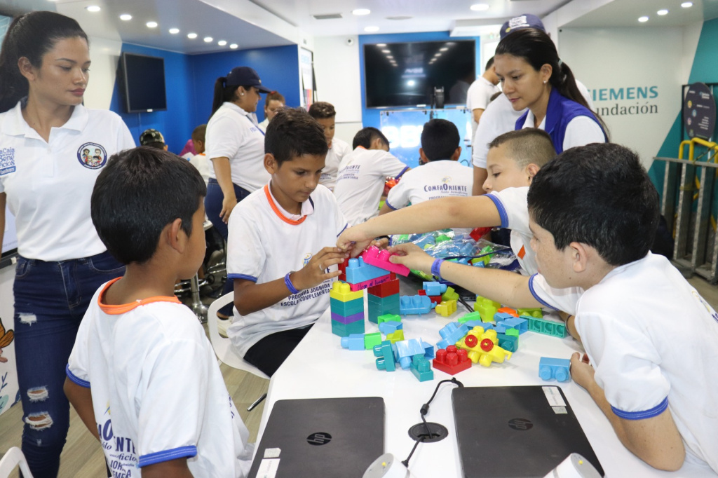 Niños en taller construyendo con bloques de plástico coloridos en una mesa, supervisados por adultas en un aula móvil.
